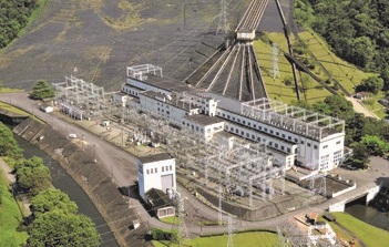 Vista aérea da usina hidrelétrica Henry Borden com prédios brancos, torres e estruturas metálicas. Atrás dela há dutos de água, e ao redor vê-se vegetação verde e um canal de água passando ao lado